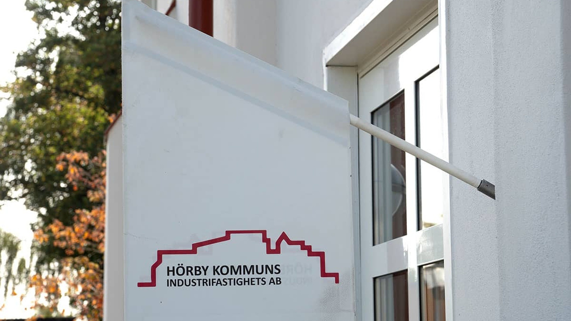 Närbild på fasadmonterad vit flagga med Hörby Industrifastighets AB:s logotyp